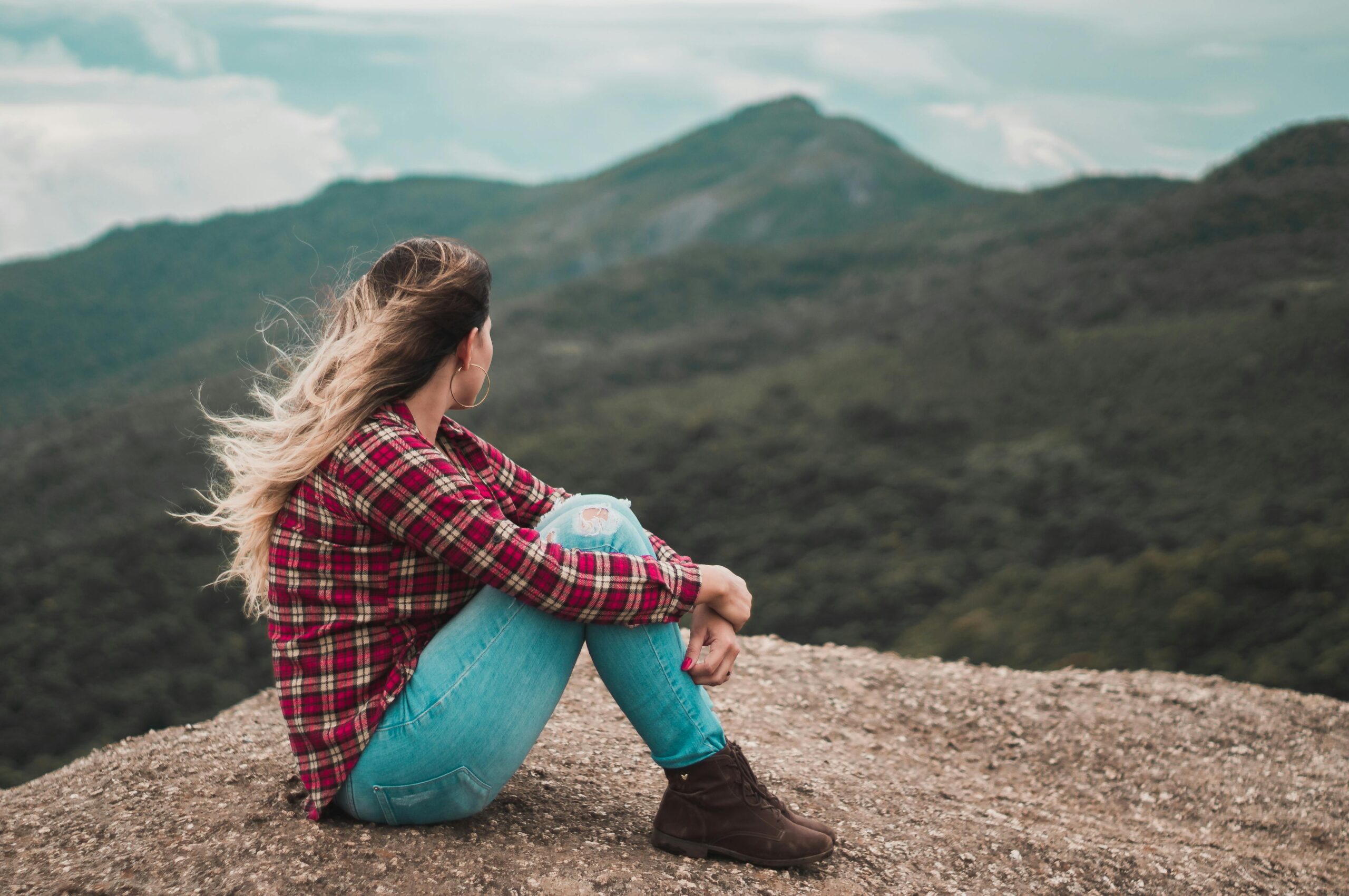 Woman sitting on cliff, perhaps, possibly asking herself the question, "Should I Use a Ghostwriter?"