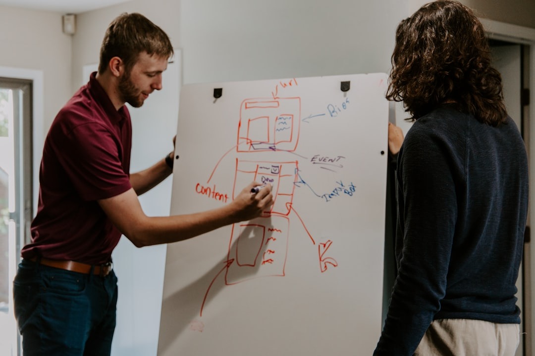 Image shows a man writing on a white board to illustrate the article topic: Writing a book outline.