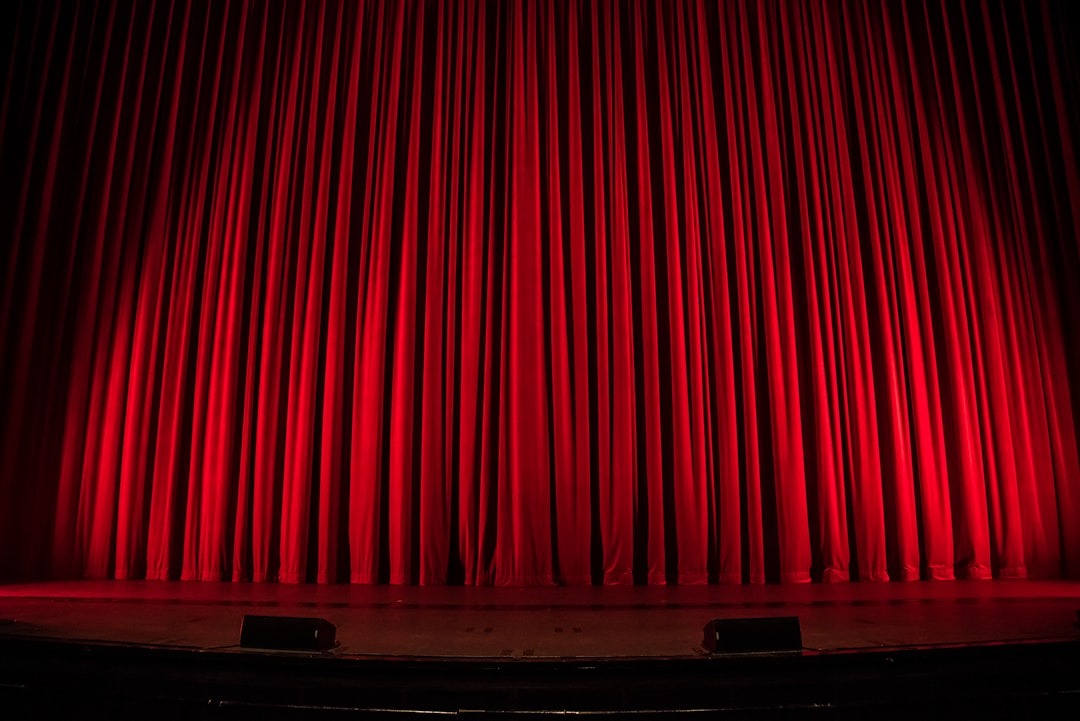 A traditional red curtain is closed in front of a stage. This is to shos the idea that ghostwriters work behind the scenes. Should authors credit their ghostwriters?